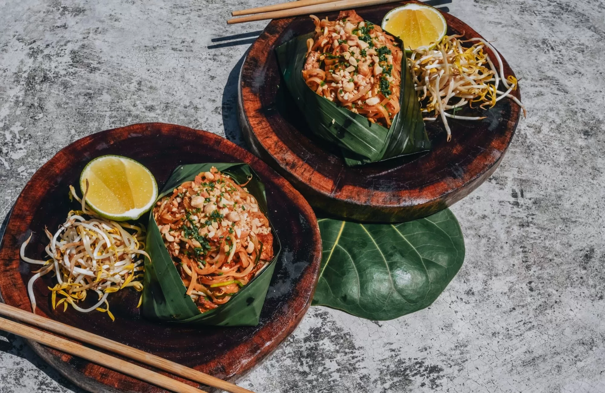 Thai noodle dishes in banana-leaf serving boats, with lime and condiments at Mezzanine.